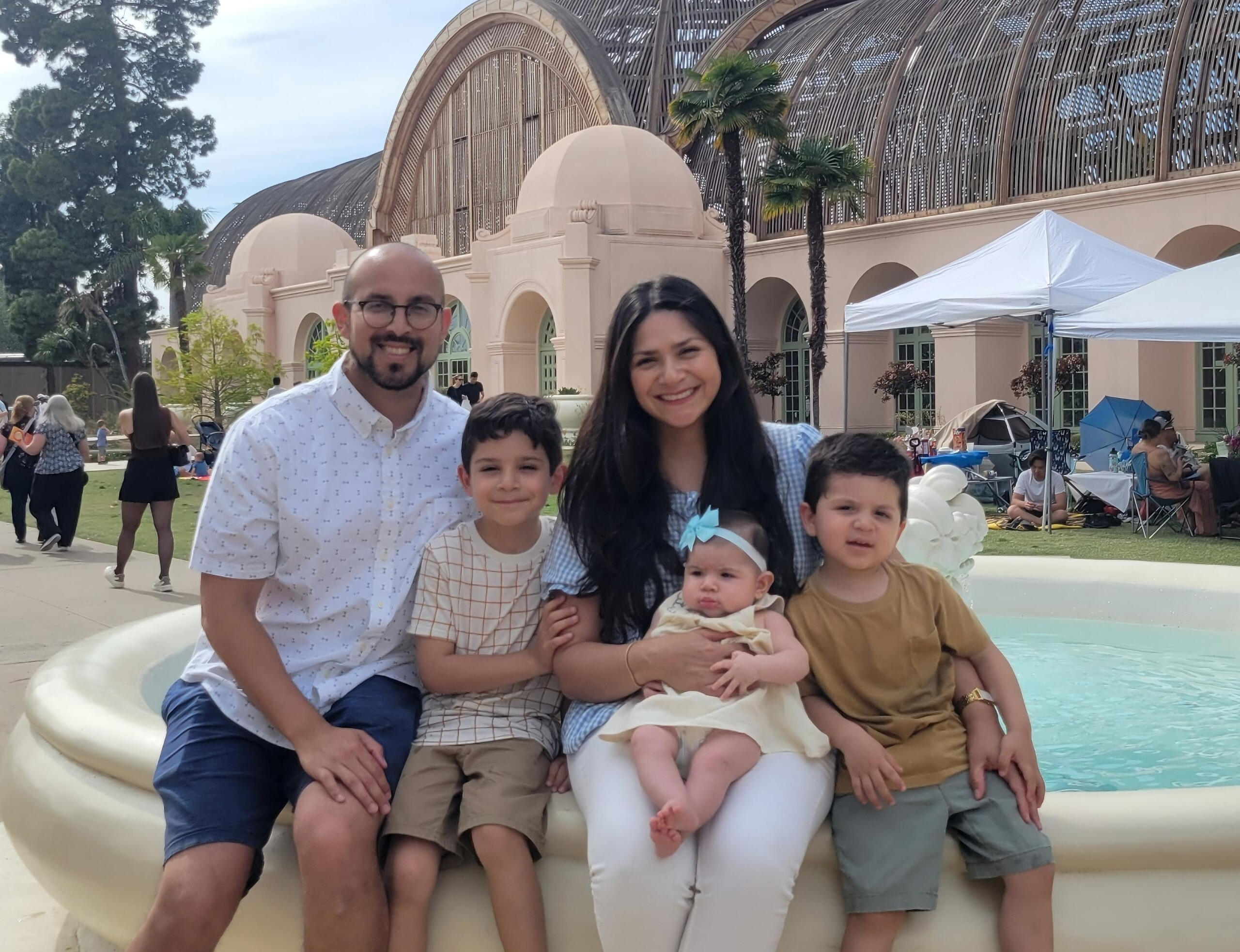 Founder's Family A photograph of the founder's, Michael Cuellar, family including his wife, two sons, and baby girl sitting on a fountain outside.